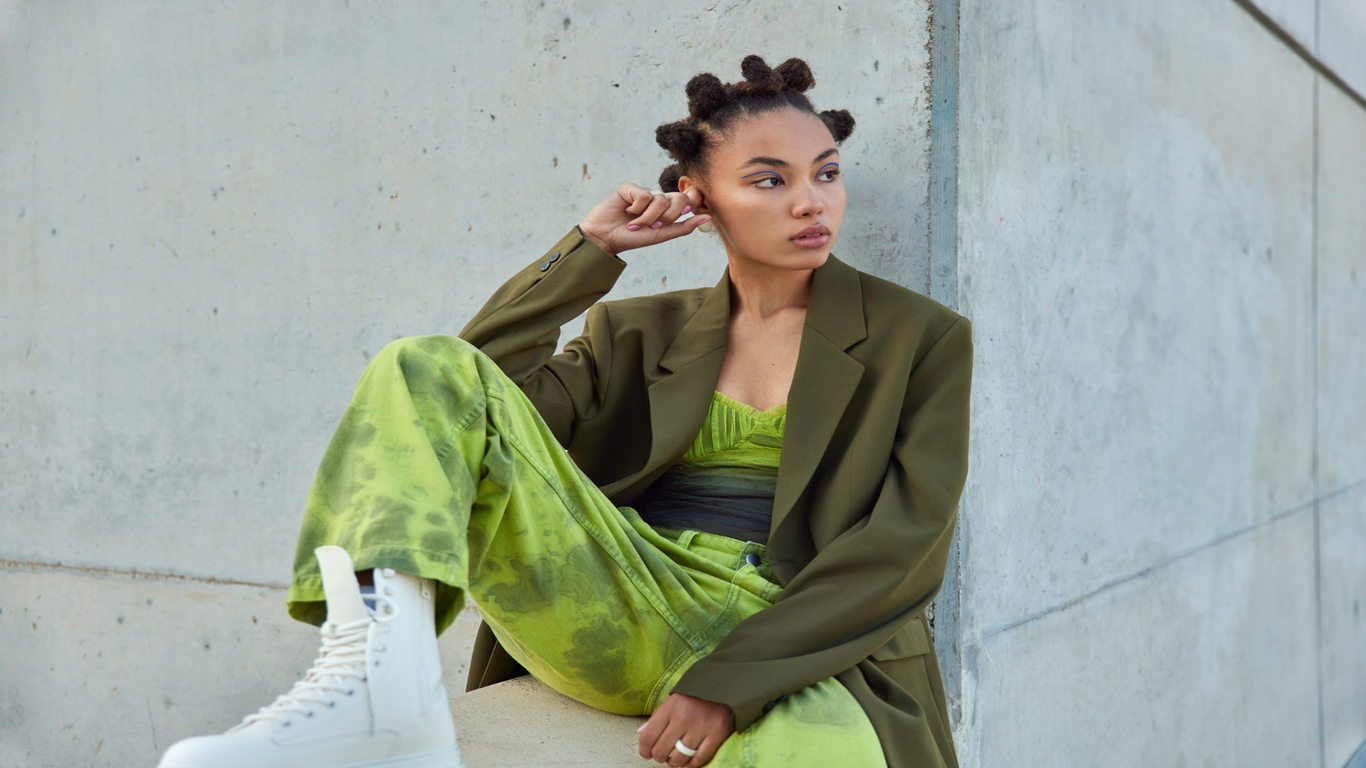 imagem de uma moça sentada com um casaco verde e um macacão verde em alusão ao estilo Athluxury