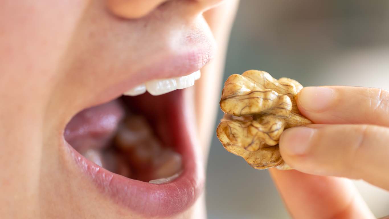 imagem de uma pessoa comendo nozes, um dos alimentos citados no texto