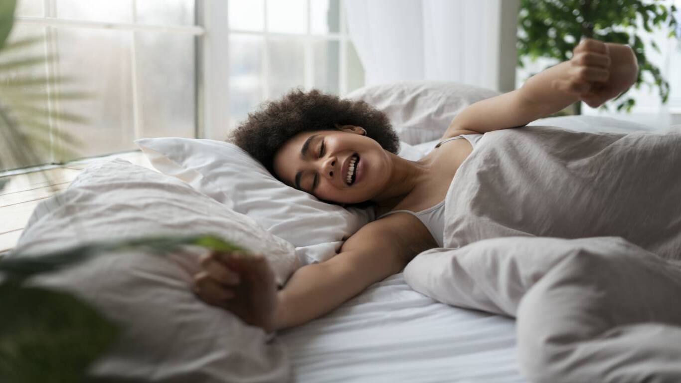 imagem de uma moça deitada em uma cama e sorrindo como se tivesse conseguido dormir bem