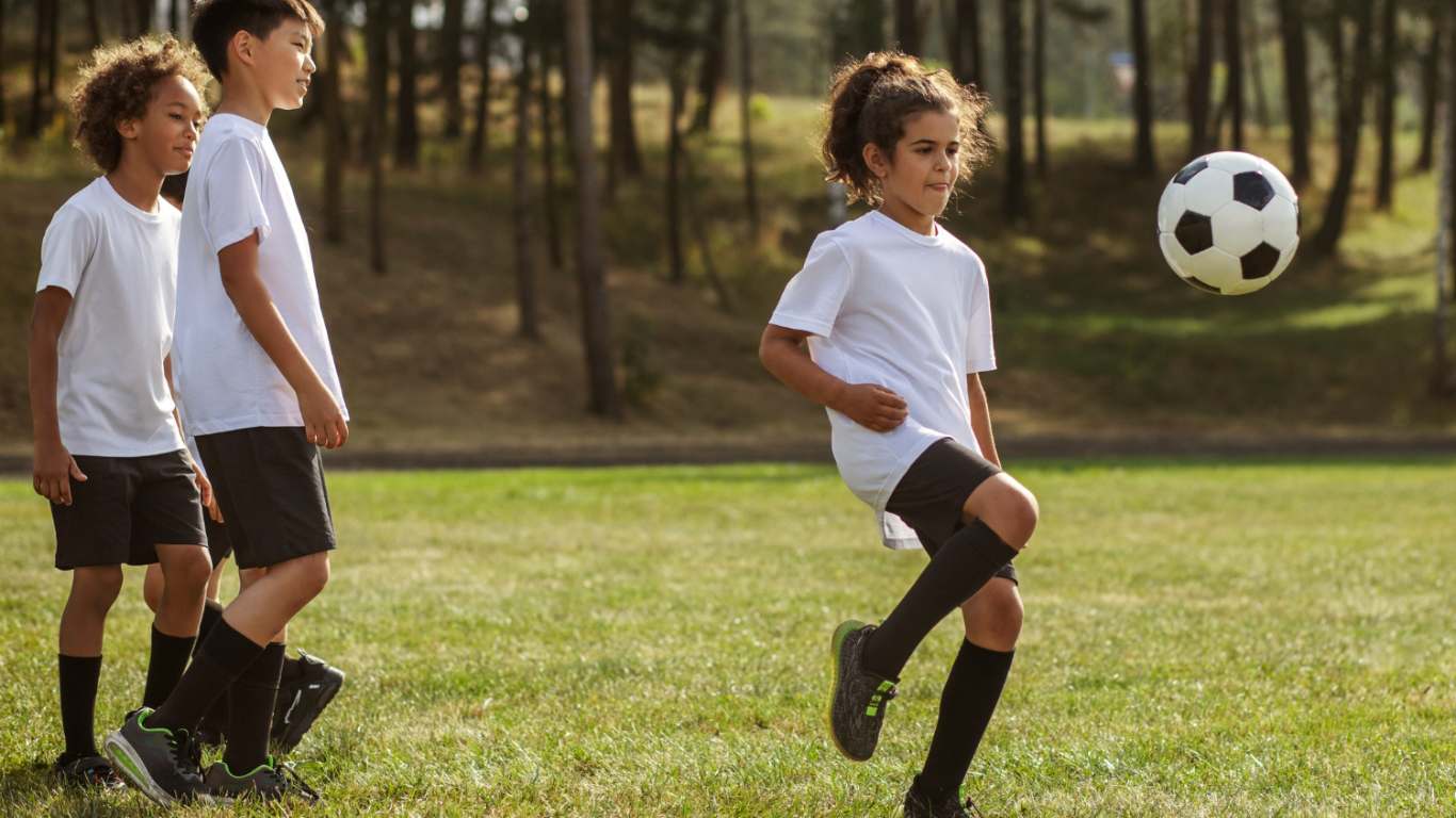 Crianças jogando futebol supervisionadas por treinador de futebol