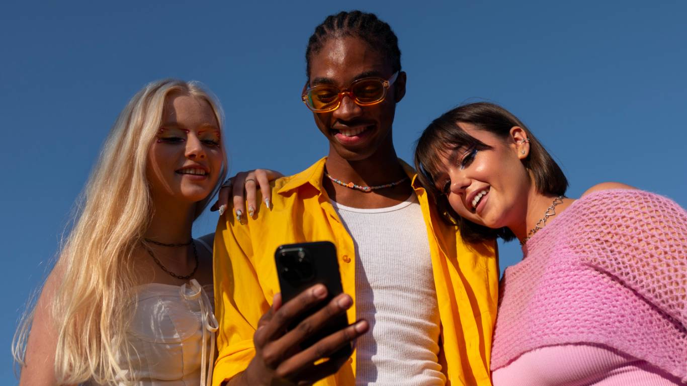 imagem de três jovens em pé olhando para um celular e sorrindo
