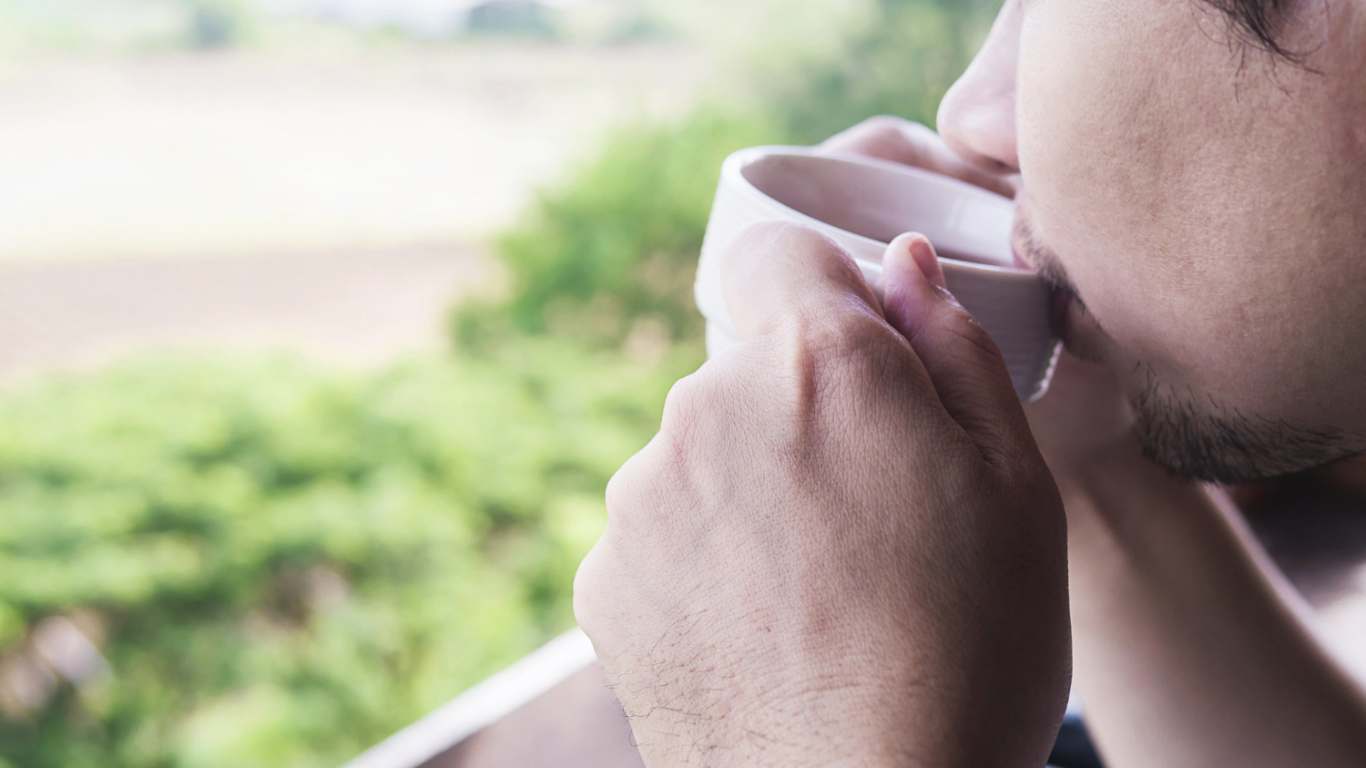 imagem de um rapaz tomando café enquanto contempla a vista para a natureza