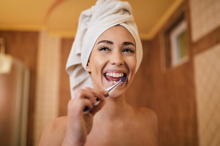 imagem de uma moça com a toalha na cabeça escovando os dentes
