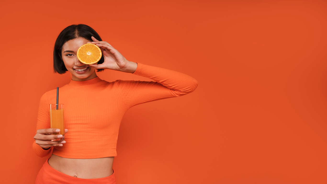 imagem de uma moça segurando uma laranja e um suco em alusão à vitamina c