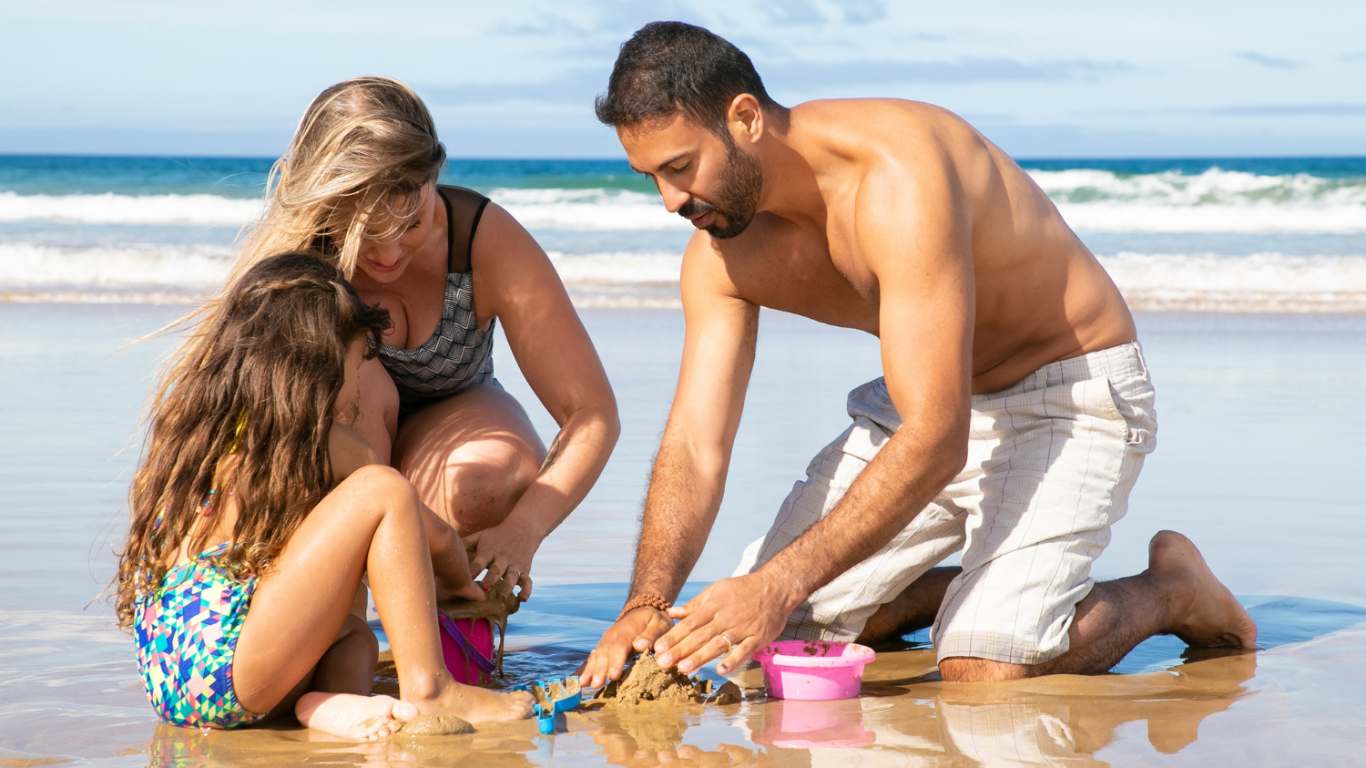 imagem de um casal brincando com a filha na praia