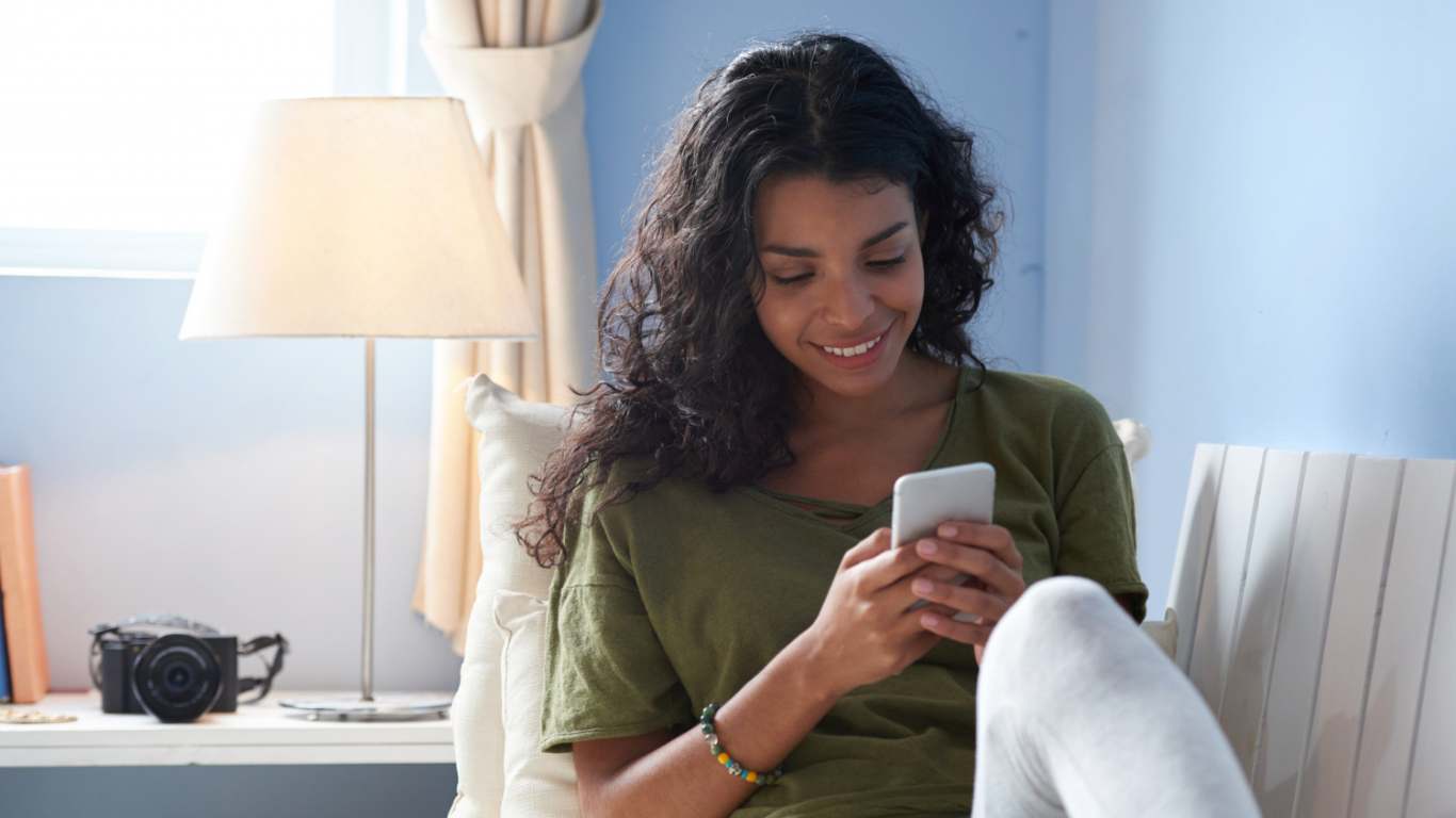 imagem de uma moça mexendo no celular e sorrindo